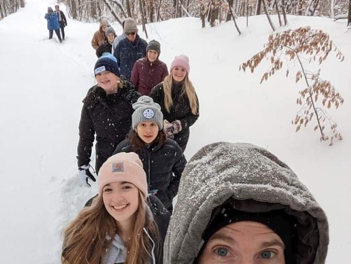 Several bundled up people hike in a line in the snow during holidays at the lake cabin