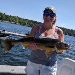 Woman with baseball cap and sunglasses holds huge walleye while on boat
