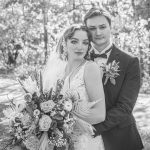 Bride and groom embrace and look serious in a black and white photo