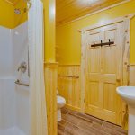 Pine wood bathroom with shower, toilet, sink, and grab bars for accessibility