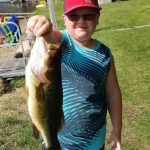 Boy with red cap and sunglasses holds a largemouth bass
