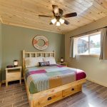 Lakeside cabin bedroom with pine ceiling, rustic pine bed, wood tile floor, and window