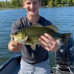 man shows off large mouth bass on boat
