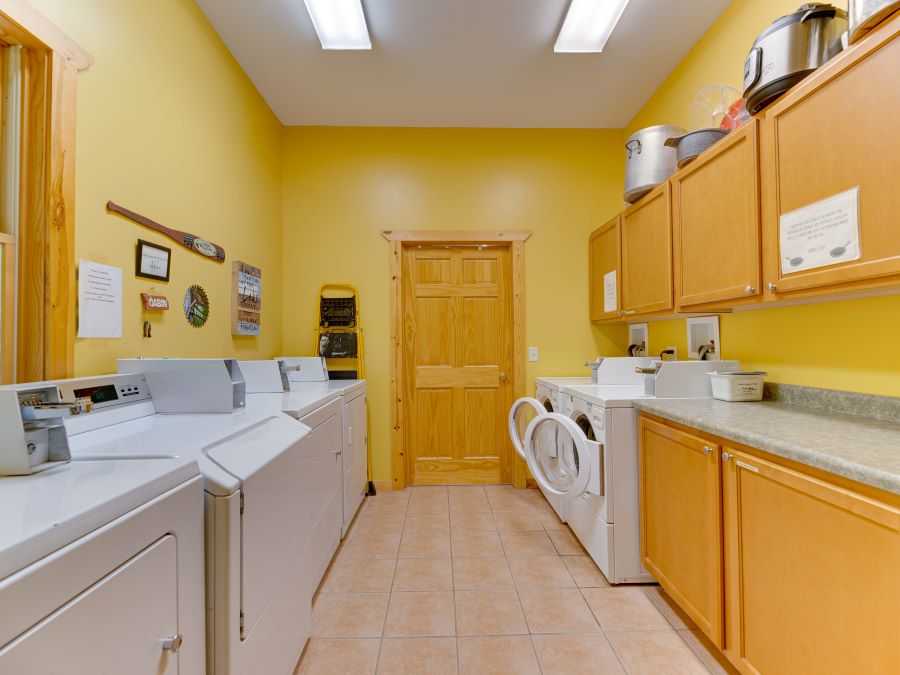 Laundromat with yellow walls and oak cabinets, 2 commercial washers and 4 commercial dryers on a light brown tile floor