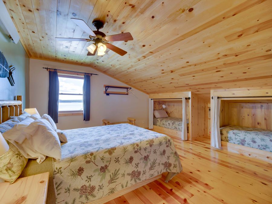 bedroom with pine cone bedspreads on a queen bed and two twin cubby beds with wood floors and ceiling