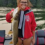 woman in red jacket on a boat hold a northern pike over 30 inches long