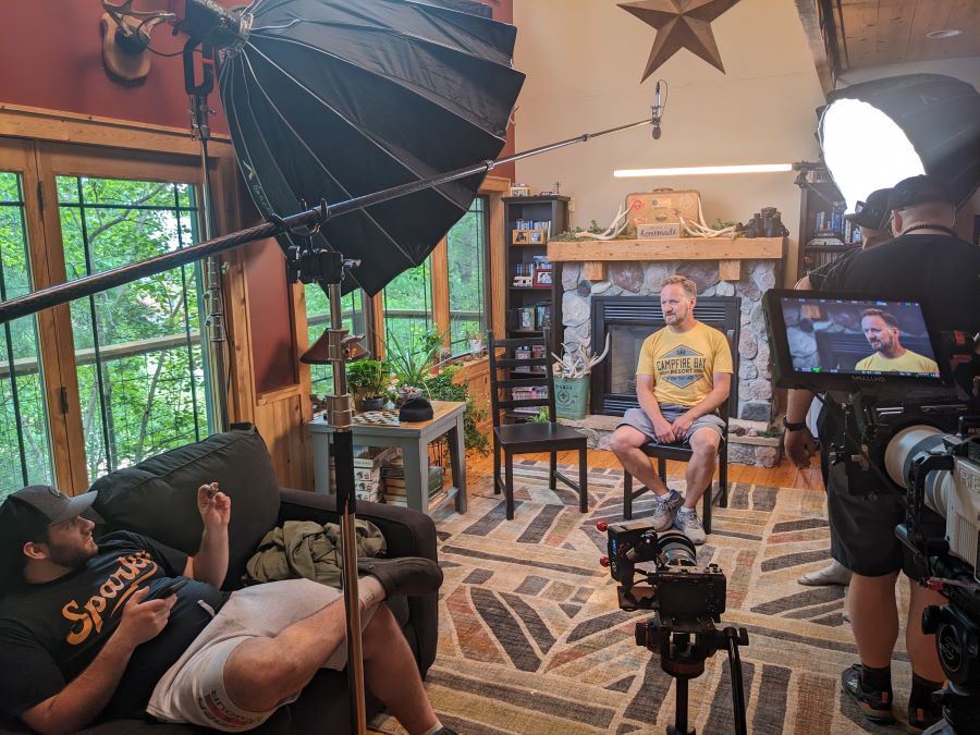 Director and videographer talk to man being filmed in a living room with cameras, lights, and black umbrellas as they film at Campfire Bay Resort