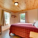 Queen bed with quilt in main floor bedroom with two windows of 4 BR cabin