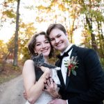Bride and Groom smile while holding their grey and white kitten while standing in the woods
