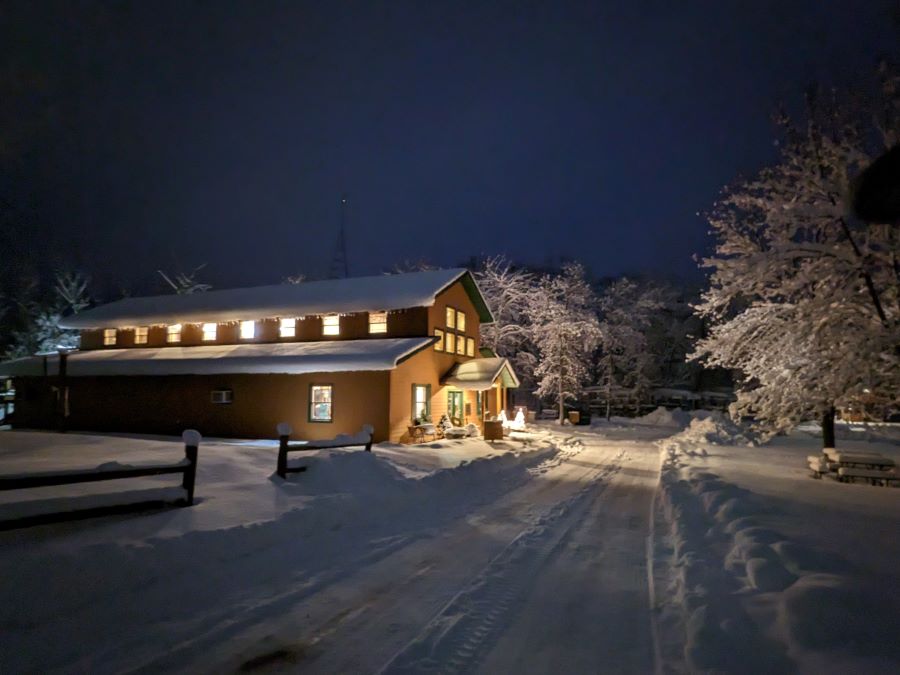 Campfire Bay Resort Lodge at night all lit up with beautiful white snow on the roof, lawn, road, and trees.