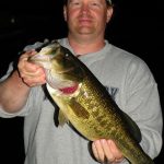 Man with cap and grey shirt holds a massive largemouth bass