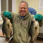 older man holds 2 huge crappie fish while in a fishing cleaning house