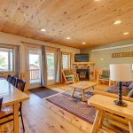 Large 4BR cabin with open concept living area with gas fireplace, covered deck off of living room, and large dining table.