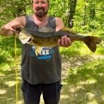 A man with a beard holds up a large walleye fish