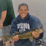 Young woman in blue hoodie holds a large walleye while on a boat