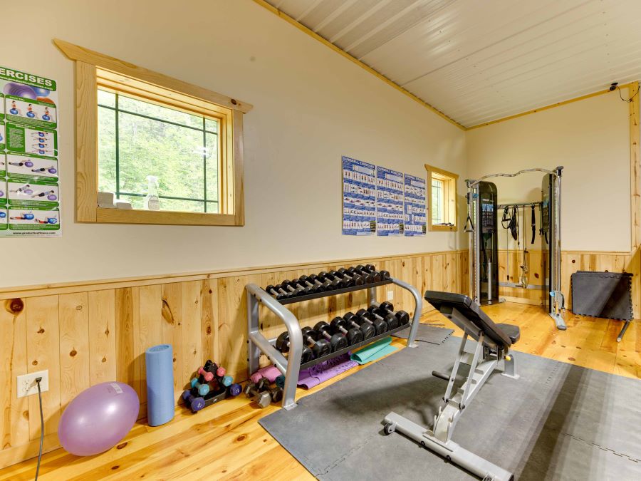 Fitness area with a functional trainer, bench, weight rack full of weights, pilates ball, posters with excercise routines, and window