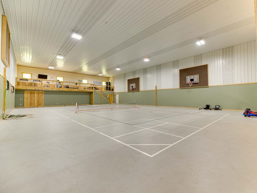 Large gym floor with basketball hoops, 2nd story open fitness room, white metal ceiling, and pine wood accents