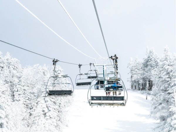 ski lift with several empty chairs and white ski run below bordered by snow covered pine trees