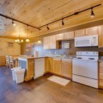 A spacious kitchen with oven, refrigerator, microwave, dishwasher, and wood looking tile floor and wood ceiling