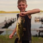 smiling boy hold largemouth bass in front of docks at Campfire Bay Resort