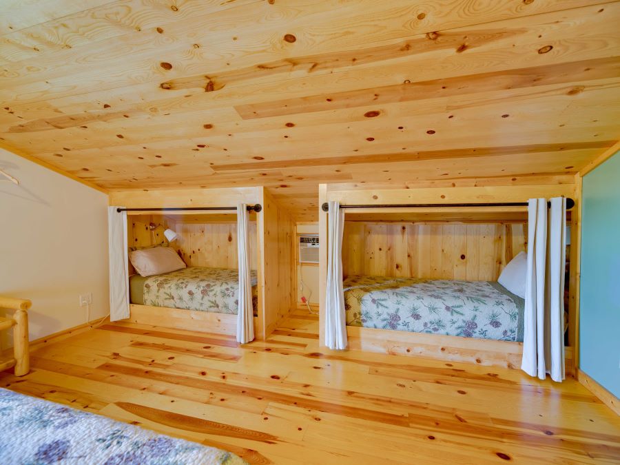 Bedroom with one queen bed and two built in twin bubby beds on third floor with wood floors and ceiling