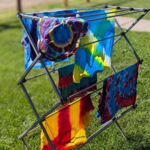Tie dyed shirts drying outside in the sun on a drying rack