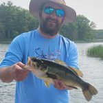 man with wide brimmed hat and reflective sunglasses holds a bass