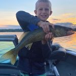 kid holds a large walley while on a boat on Fish Trap Lake at sunset