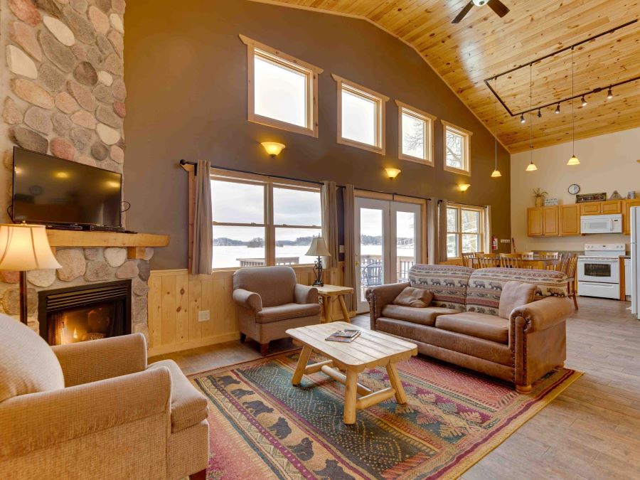 Romantic cabin with living, kitchen, and dining room, stone fireplace and large lake-facing windows and high ceilings