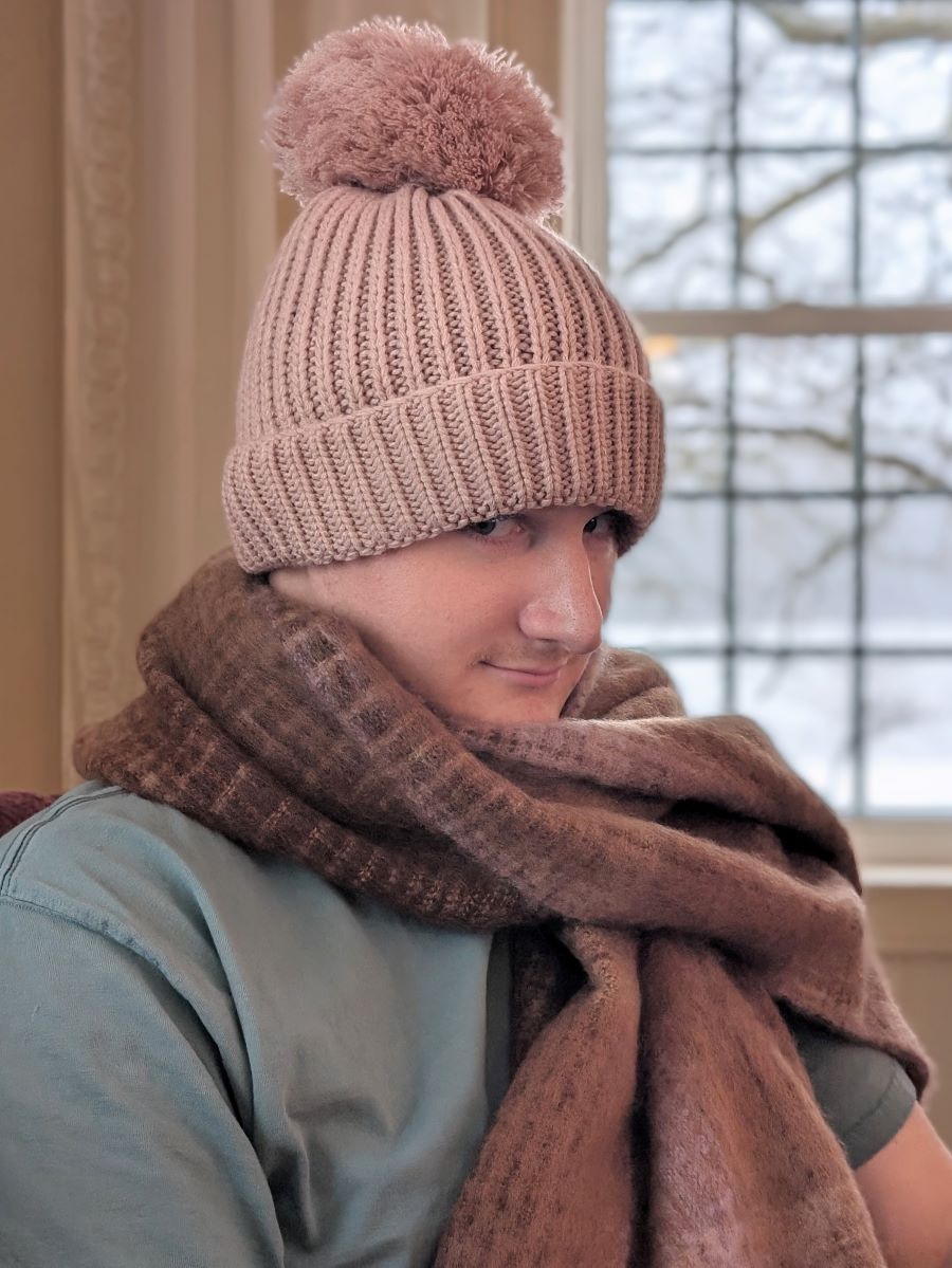 A young man poses in pink winter hat and scarf that were Christmas gifts