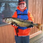 Boy with ball cap, orange hoodie, and blue life vest holds a huge walleye fish