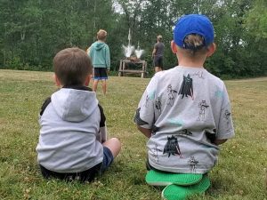 two young boys sit in the grass watching 2 bottle rockets launch during resort activity