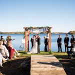 A bride and groom kiss under a chuppah at a Jewish and Christian wedding ceremony on a lake