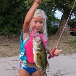 young blond haired girl holds up a largemouth bass
