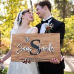 Bride and groom hold a handmade wooden sign with laser cut letters forming the words "The Sams Family--est. 2023"