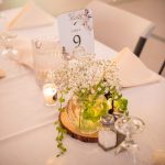 Table setting at a wedding reception includes wood slab with flowers, table number and candles