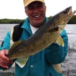 Man with yellow cap and green jacket holds a large walleye while on the lake