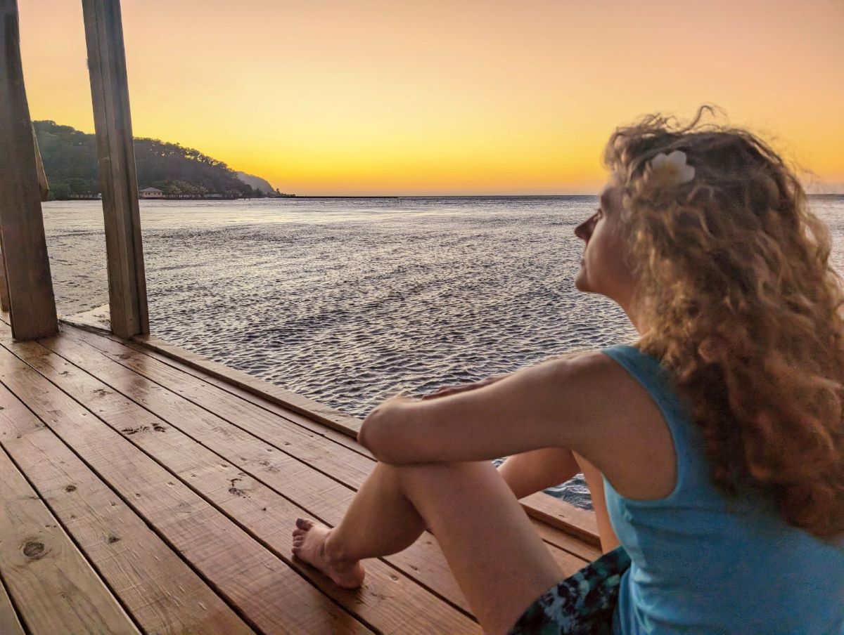 A woman sits on a dock at sunset reflecting what she wants her future to look like before creating her roadmap to goal achievement. 