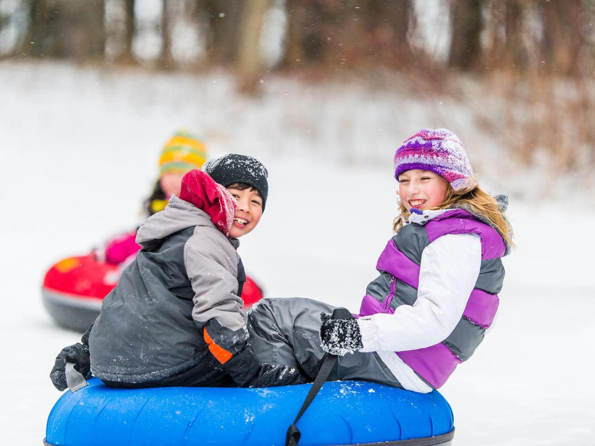 Two smiling kids tube down a hill in the snow because tubing is one of the top things to do in the Brainerd Lakes Area in the winter