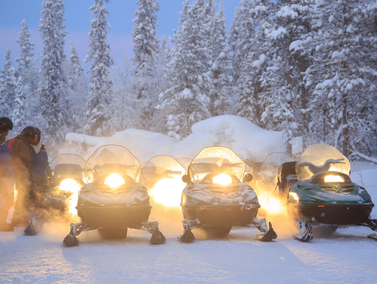 Snowmobiles with their lights on in the snow covered forest, like in the Brainerd Lakes Area
