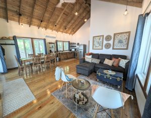 Tropical island rental cabin living area has a sleeper sofa, side chairs, a dining set that seats 6, and a full kitchen