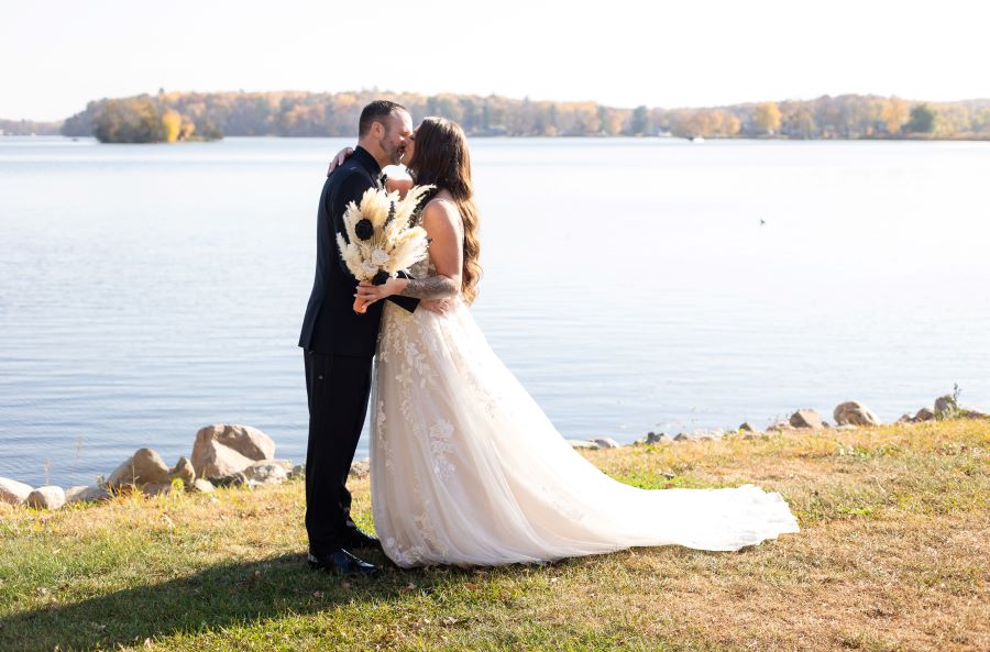 A lakeside resort wedding couple kiss in the autumn sunshine.