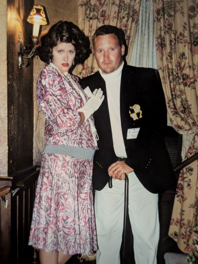 A man dressed as a sea captain and a woman in a silk dress and bobbed curly hair pose at a murder mystery party