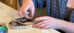 a close up of a woman's hands as she places an element on a collage piece.