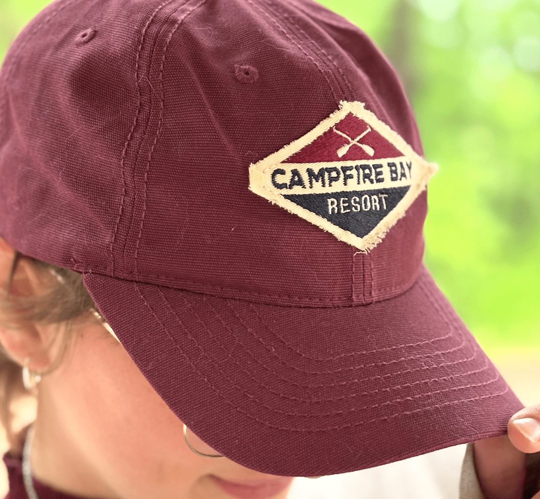 A woman wears a ball cap embroidered with "Campfire Bay Resort" on a sunny day.