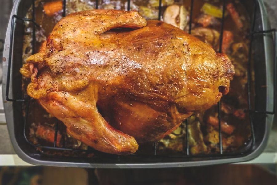 A turkey in a pan, on a bed of roasted veggies.