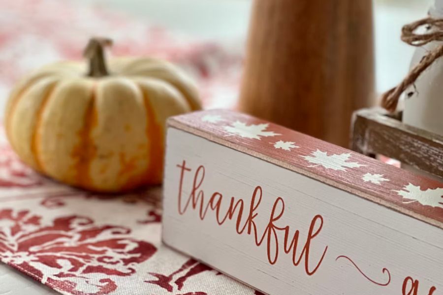 A sign that says "thankful" sits on a tablecloth beside a small pumpkin.