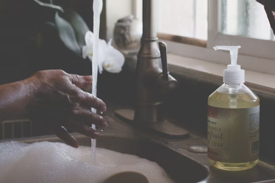 A person washes their hands and dishes in a sink with bubbles.