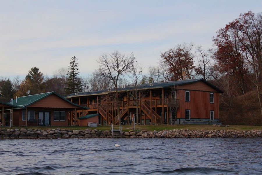 A dark shot of a grouping of cabins from the lake. The water is wavy, and the sky is clouded.