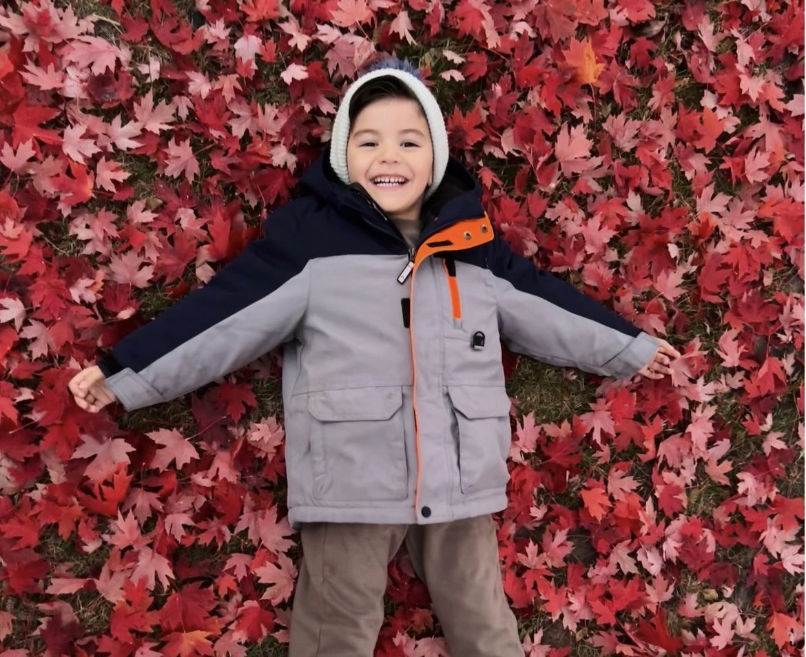 Image of little boy laying on top of red maple leaves